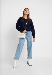 Námořnický cropped svetr, světle modré široké džíny s vysokým pasem, bílé kotníkové boty a malá krémová crossbody taška se zlatým akcentem.