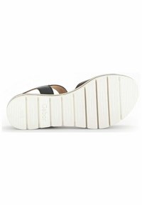 Sandale en cuir noir avec de larges sangles, dos fermé, et une semelle en caoutchouc blanc texturé avec un motif strié et une étiquette de marque.