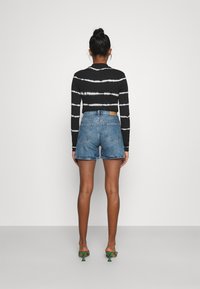 Camiseta negra de manga larga con rayas de tie-dye blanco, combinada con pantalones cortos de denim azul de cintura alta y sandalias verdes de tacón.
