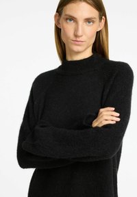 Schwarzer Strickpullover mit hohem Kragen, lockerer Passform und langen, weiten Ärmeln. Weiche Textur mit leicht flauschigem Aussehen.