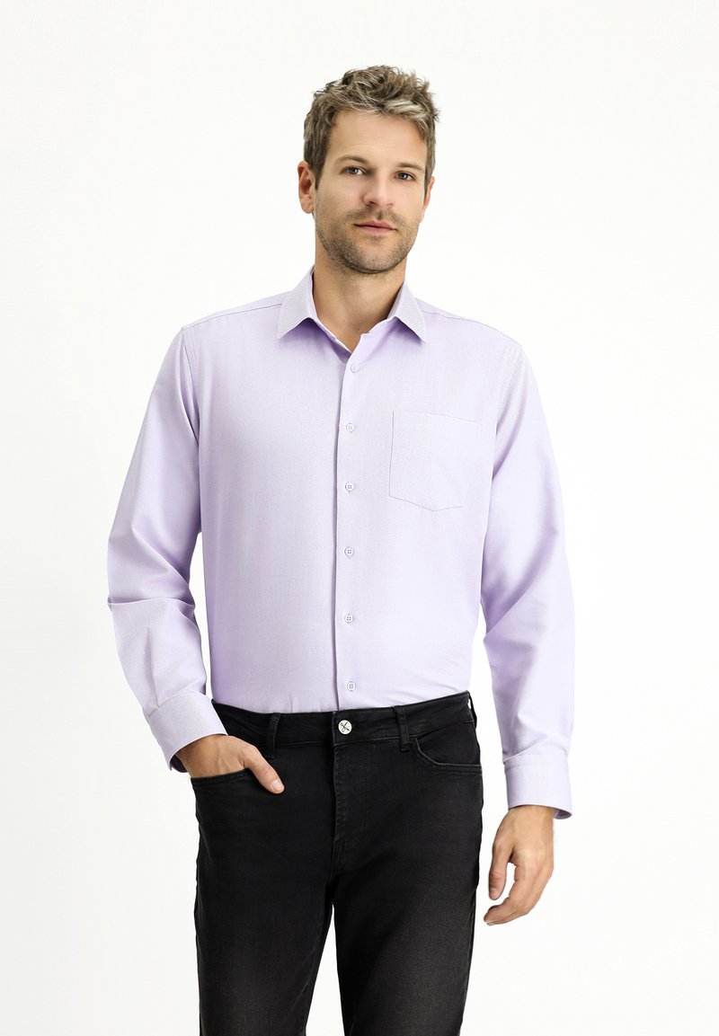Camicia button-up di un leggero colore viola con maniche lunghe e taschino sul petto, abbinata a jeans neri. Tessuto soffice e design classico.