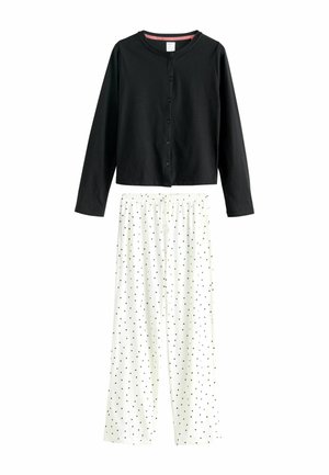 Schwarzes langärmliges Button-Down-Oberteil kombiniert mit weißen weit geschnittenen Hosen, die ein schwarzes Pünktchenmuster und einen elastischen Bund haben.
