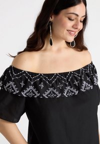 Schwarze schulterfreie Bluse mit einem strukturierten elastischen Ausschnitt und weißen gestickten geometrischen Mustern im oberen Bereich.