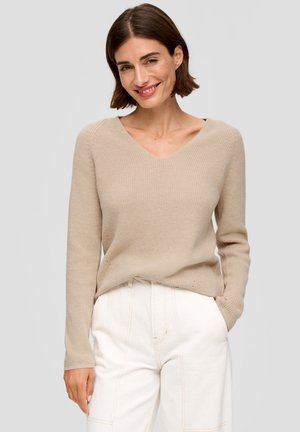 Beige v-neck sweater made of textured knit fabric, paired with high-waisted white pants. Sweater features long sleeves and relaxed fit.