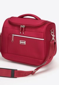 Borsa da viaggio rossa con texture, dotata di doppie cerniere, tasca frontale e tracolla regolabile. Presenta una placca logo in metallo e un manico imbottito.