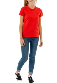 Camiseta de algodón roja con escote redondo y mangas cortas, combinada con jeans ajustados azules y zapatillas negras con rayas blancas.