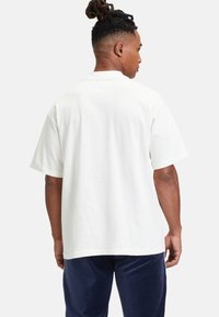 Biała bawełniana koszulka z krótkim rękawem, luźny krój, okrągły dekolt i gładka tekstura. Widok z tyłu nie pokazuje wzorów ani grafiki.