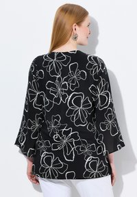 Blusa nera floreale con motivi di fiori ricamati bianchi, maniche a campana e vestibilità rilassata. Tessuto liscio e materiale leggero.