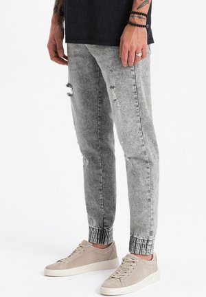 Faded gray jeans with distressed detailing, slim fit, and elastic cuffs. Paired with soft beige sneakers.