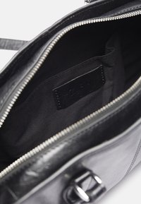 Wnętrze czarnej skórzanej torby z zamknięciem na zamek, charakteryzujące się gładką teksturą, podszewką z materiału oraz małą metką wewnątrz.