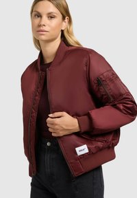 Bordeaux bomberjack met een gladde textuur, geribde manchetten, een ritszak op de mouw en een logo label aan de zoom.