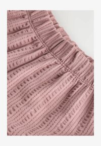 Tela rosa suave acanalada con una cintura elástica fruncida y rayas verticales texturizadas sobre un fondo liso.