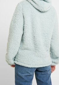 Fuzzy ljusblå hoodie tillverkad av texturerat, mjukt material. Har en huva och lös passform, med en något kortad kant och vida ärmar.