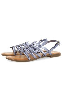 Sandalias metálicas azules con tiras trenzadas y diseño de punta abierta. Suela plana con plantilla de cuero marrón y correa ajustable en el tobillo.