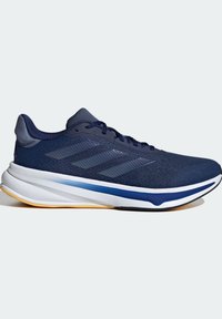 Chaussure de course bleu marine avec trois bandes foncées, semelle blanche et bleue, bande de roulement jaune et fermeture à lacets sur un fond uni.