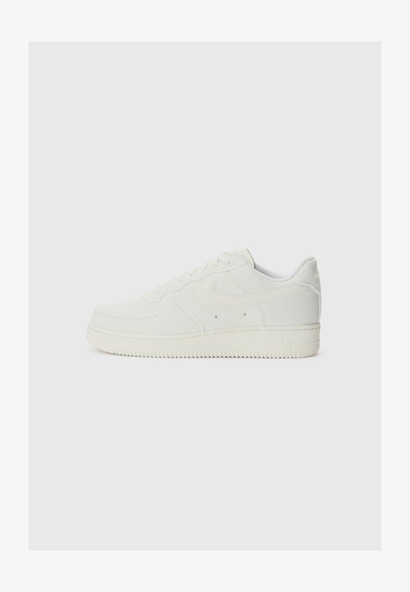 Adidași albi Nike Air cu un superior din material texturat, vârf rotunjit, șireturi în față și branding embosat pe călcâi.