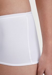 Witte katoenen hipsteronderbroek met een gladde textuur, elastische tailleband en contrasterende stiksels langs de naden. Close-up zijaanzicht.