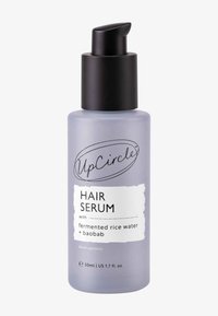 Lila frostad glasflaska med svart pump. Etiketten lyder "Hair Serum med fermenterat risvatten + baobab," 50 ml kapacitet.