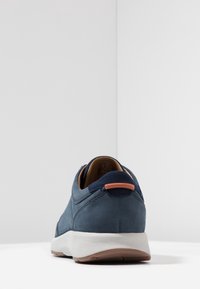 Mörkblå sneakers med en texturerad ovansidan, mjuk foder och en vit sula. Distinkt orange detalj på hälen ger extra karaktär.