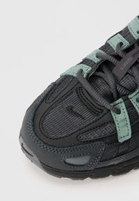 Czarne sneakersy z teksturowanej tkaniny, z akcentami z zielonego zamszu i kontrastującą ciemną gumową podeszwą. Posiadają sznurowaną konstrukcję z wzmocnionymi obszarami.