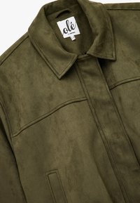 Chaqueta de ante verde oliva con cuello puntiagudo, dos bolsillos horizontales en el pecho y una textura suave con un ligero brillo.
