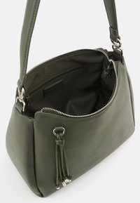 Olive green leather handbag with a zip closure, tassel detail, and metal hardware. Interior features a solid fabric lining and pocket.