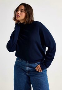 Mörkblå polotröja i mjukt tyg med avslappnad passform, kombinerad med högmidjade blå jeans. Långa ärmar, enkel design.