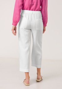 Weiße Leinen-Culotte mit bequemem Schnitt, ausgestattet mit Gesäßtaschen und einem weichen, elastischen Bund, kombiniert mit einer lebhaften pinken Bluse.