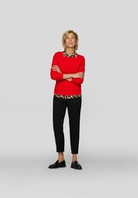 Roter Pullover über einem Tiermotiv-Hemd mit Kragen, kombiniert mit schwarzen, schmal geschnittenen Hosen und glänzenden schwarzen Mokassins. Einfaches Design, strukturierte Materialien.