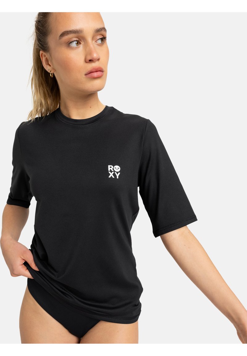 T-shirt de manga curta preta, feita de material elástico, com um pequeno logótipo branco da Roxy no peito e detalhes canelados na bainha.