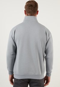 Suéter de tiro alto en gris claro, con cuello alto, mangas largas y puños y bajo acanalados. Hecho de una suave tela texturizada.