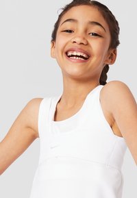 Λευκή αθλητική αμάνικη μπλούζα με στρογγυλή λαιμόκοψη, που διαθέτει ένα διακριτικό λογότυπο της Nike. Το υλικό φαίνεται ελαφρύ με απαλό texture.