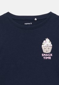 Μπλε ναυτικό πουκάμισο με γραφικό εν ός κεκάκι που χαμογελά, με καρδιές στην κορυφή και το κείμενο "SNACK TIME" κάτω από αυτό στο στήθος.