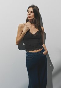 Melna mežģīņu apakškrekls ar regulējamām plānām lencēm, kombinēts ar augsta vidukļa tumšām džinsu biksēm ar brīvu piegriezumu un priekšējām kabatām.