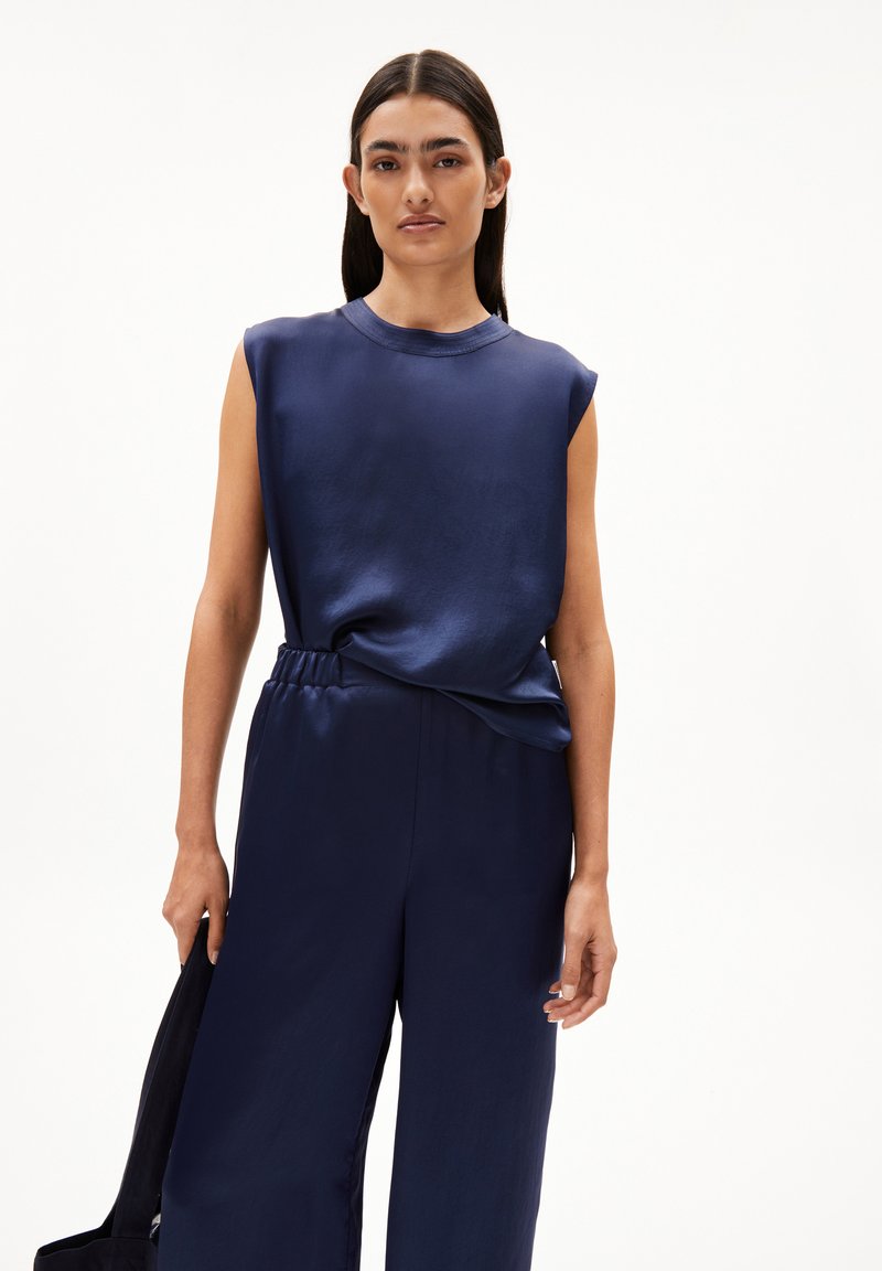 Navy sleeveless top with a round neckline, paired with navy wide-leg trousers. Both garments have a smooth, shiny texture and a relaxed fit.