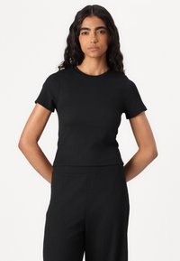 Black short-sleeve top with a textured fabric, fitted design, round neckline, and seamless hem, paired with matching high-waisted pants.