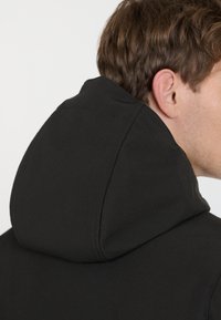 Black hoodie with a rounded hood, smooth texture, and visible stitching details. The garment is seen from the back, highlighting the hood's shape.