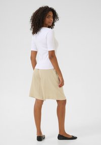 Haut blanc à manches courtes associé à un short beige jusqu'aux genoux et des ballerines noires. Texture lisse, coupe décontractée et détails de design subtils.