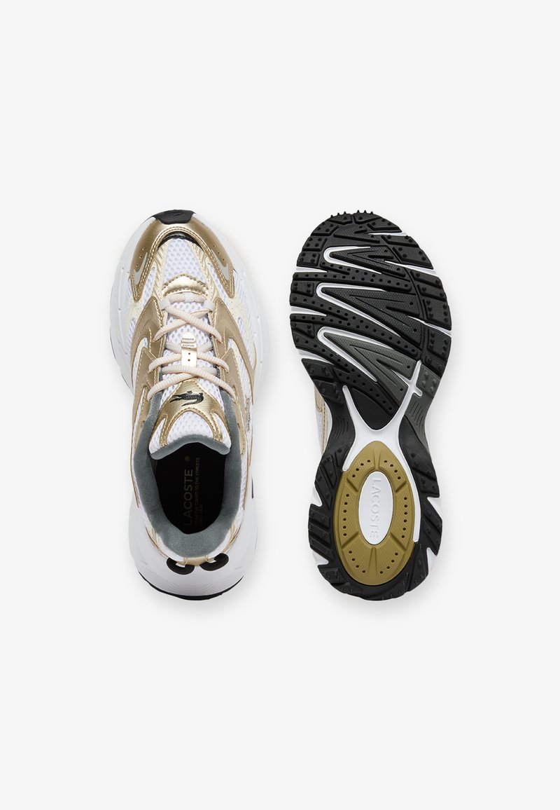 Gold and white athletic shoes with a mesh upper, padded collar, and rubber outsole featuring a textured black pattern. LACOSTE branding visible.