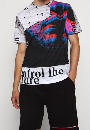 Homme portant un t-shirt graphique à manches courtes avec un design abstrait rouge, bleu, noir et blanc et le texte "control the future,", associé à un short noir.