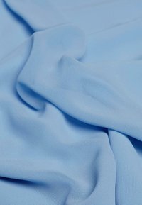 Hellblauer Stoff mit glatter Textur, der subtile Drapierungen und Falten aufweist. Das Material wirkt leicht und weich.