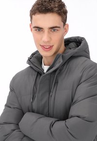 Szürke tollkabát kapucnival, steppelt mintával, elöl cipzárral és állítható húzózsinórokkal. Simább tapintású és szigetelt fazon.