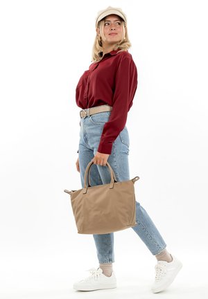 Beigefarbene Tragetasche mit zwei Griffen, aus weichem Material gefertigt, mit glatter Textur. Getragen zu hoch taillierten blauen Jeans und weißen Sneakers.