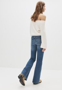 sweater u obliku kupole boje svijetle kreme, plave traperice s zvonastim rezom, čizme do gležnja, teksturirana pletenina, srednji struk, suptilno izbljeđivanje na trapericama i šivene stražnje džepove.
