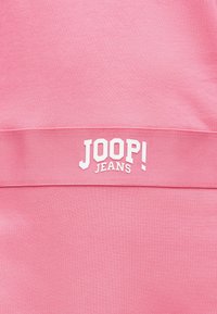 Ροζ ύφασμα με οριζόντια υφασμένη ταινία που φέρει το λευκό λογότυπο της μάρκας "JOOP! JEANS" στο κέντρο της.