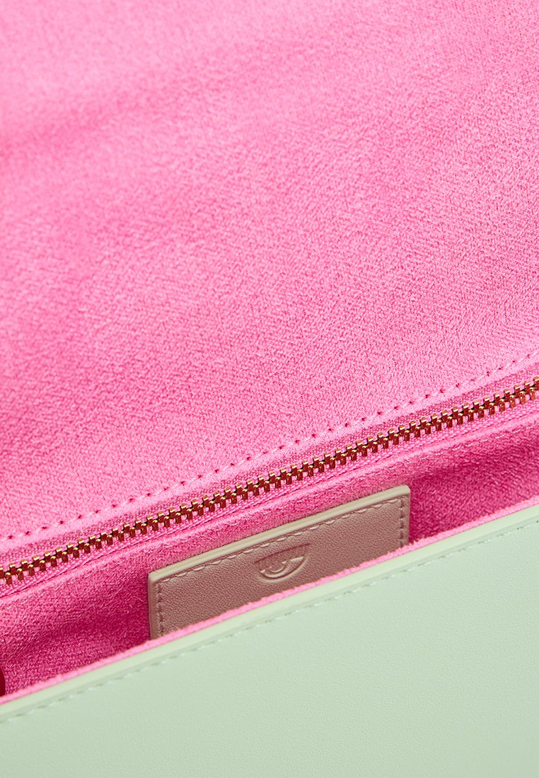 Interior de un bolso de cuero verde que muestra un forro de ante suave rosa, con una cremallera dorada y un tarjetero marrón claro ubicado dentro.