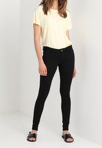 Gelbes Kurzarm-T-Shirt kombiniert mit engen schwarzen Jeans und schwarzen Sandalen. Glattes Material, einfaches Design und keine Muster oder Akzente.