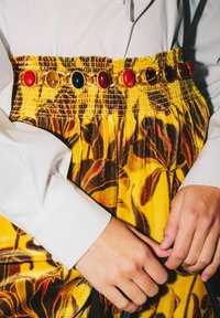 Pantaloni in velluto giallo con motivo floreale, dotati di una vita arricciata decorata con pietre preziose ovali colorate in rosso, nero e accenti dorati.
