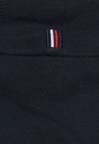 Tela azul marino con una textura suave que presenta un pequeño logo bordado con rayas verticales en rojo, blanco y azul cerca de la costura.