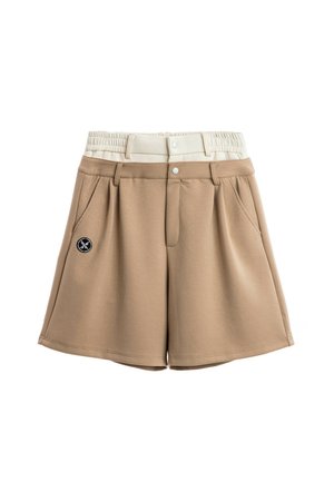 Joven con rastas que lleva una camiseta deportiva grande de España en azul marino, pantalones cortos beige, calcetines blancos y botas de trabajo color marrón claro, de pie contra un fondo blanco.